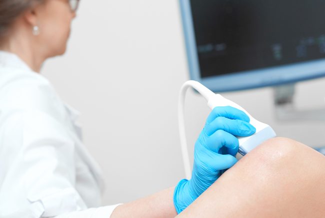 Cropped close up of a female doctor using ultrasound scanner examining injured knee of her patient pain arthritis injury healthcare medicine profession occupation technology.